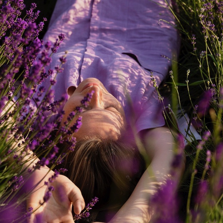 Mujer acostada en un campo de lavandas en flor, disfrutando de un momento de relajación y conexión con la naturaleza en un ambiente sereno gracias a Ka Wellness Coach Online